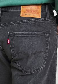 Lähikuva mustast Levi's teksapüksi tagakoti, kus on nähtav punane silt ja nahkbrändi etikett koos õmblusdetailidega.