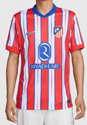 Uomo che indossa la maglia da calcio a righe rosse, bianche e blu dell'Atlético Madrid con il logo Nike e il logo dello sponsor Riyadh Air sul davanti.