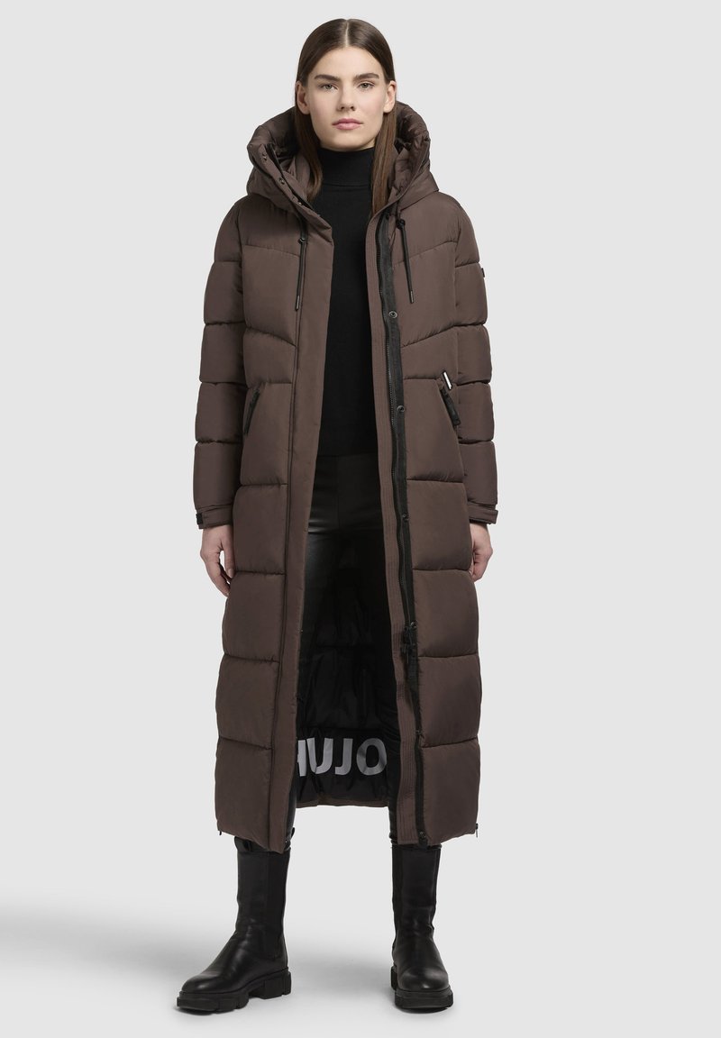 Brūns garš pūšamo mēteli ar kapuci, ar iešūtiem laukumiem, rāvējslēdzēja kabatām un melnu iekšpusi ar baltu zīmolu. Gluda, izturīga materiāla.