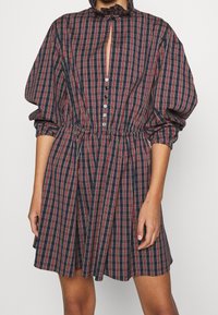 Marinrutig klänning med röda och vita ränder, med puffärmar, en volangkrage och en knappstängning framtill med en öppning.