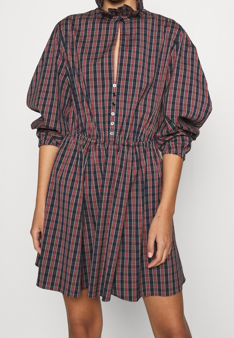 Marinrutig klänning med röda och vita ränder, med puffärmar, en volangkrage och en knappstängning framtill med en öppning.