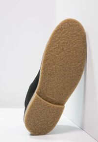 Chaussure noire avec une semelle texturée ; la semelle extérieure est marron clair et en caoutchouc, avec une finition lisse et de légers motifs pour l'adhérence.