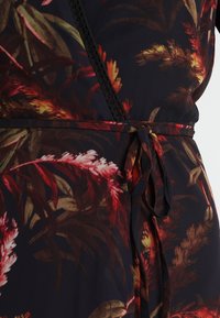 Květnatá zavinovací šaty s tmavým pozadím a živými červenými a zelenými listovými vzory. Obsahuje tónový opasek a krajkové detaily.