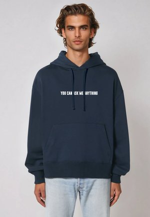 Sweat à capuche bleu marine en tissu doux avec une poche frontale. Il arbore le texte blanc "VOUS POUVEZ ME DEMANDER N'IMPORTE QUOI" sur la poitrine.