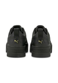 Sneaker in pelle nera con suola spessa, dotate di un accento del logo dorato e dettagli testurizzati sul tallone. Il motivo del battistrada è visibile.