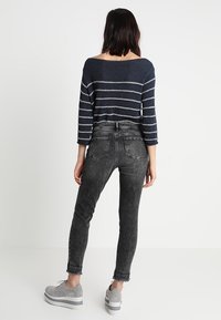 Top de manga larga a rayas marineras con escote amplio, combinado con jeans skinny negros de talle alto con dobladillo deshilachado y bolsillos traseros.