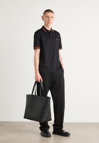 Polo shirt noir avec des détails rouges, pantalon noir et un grand sac fourre-tout en cuir noir. Tissu lisse, coupe décontractée et détails de marque minimalistes.