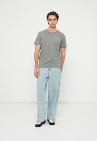 Γκρι βαμβακερό μπλουζάκι με κοντά μανίκια, στρογγυλή λαιμόκοψη και μικρό λογότυπο. Συνδυάζεται με ανοιχτό μπλε φαρδιά τζιν παντελόνια και μαύρα παπούτσια.