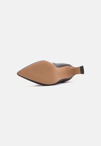 Spitz zulaufender Schuh mit einem glatten, braunen Lederoberteil, einer sandfarbenen Gummisohle und einem schmalen, schwarzen Absatz. Verfügt über eine strukturierte Außensohle für besseren Halt.