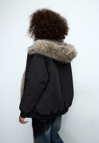 Czarna, oversize'owa kurtka z kapturem z sztucznego futra. Posiada ściągacze na rękawach, obszerny krój oraz gładkie, matowe wykończenie tkaniny.