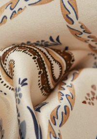 Zijde stof met intricate paisley patronen in bruin, blauw en roomkleur, met een gladde textuur en zachte val, wat de decoratieve aantrekkingskracht versterkt.