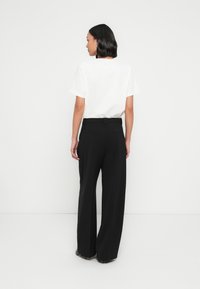 T-shirt blanc à manches courtes, associé à un pantalon large noir avec ceinture et poches arrière. Tissu lisse avec une coupe structurée.