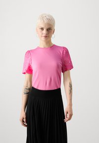 Fitted pink t-shirt with short, scalloped sleeves featuring eyelet cutouts, paired with a black pleated skirt and a wide waistband.