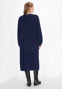 Dunkelblaues, oversized gestricktes Kleid aus flauschigem Material, mit langen Ärmeln und gerader Silhouette, das bis unter das Knie reicht.