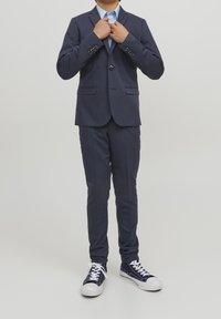 Blazer azul marino y pantalones a juego hechos de tela lisa, combinados con una camisa azul claro y zapatillas blancas con detalles en azul marino.