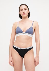Calvin Klein bh i lys lilla med en hvit kant, med en ribbet tekstur. Kombinert med svarte truser, dekorert med en hvit logo-bånd.