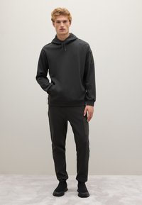 Felpa grigio scuro e pantaloni della tuta abbinati realizzati in tessuto morbido. La felpa ha un cappuccio e maniche raglan; i pantaloni presentano tasche laterali.