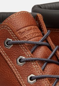 Close-up van een waterdichte bruine leren Timberland-laars met grijze veters die door metalen oogjes zijn geregen en een gevoerde donkere kraag.