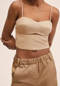 Top court beige à fines bretelles, avec un décolleté courbé et un détail découpé. Associé à un pantalon large beige taille haute.