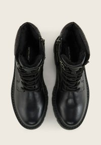 Botas de cuero negras hasta el tobillo con un collar texturizado, cordones en el frente, cremallera lateral y suela de goma. Aislamiento de forro polar visible en el interior.