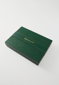 Groene kartonnen doos met een paisleypatroon, voorzien van een gouden logo "GANT" en een bijpassende groene band. Gladde textuur, rechthoekige vorm.