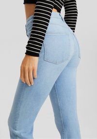 Jeans de tiro alto color azul claro con un corte ajustado, que presentan bolsillos traseros y costuras cuidadas, complementados por una blusa de manga larga a rayas negras y blancas.
