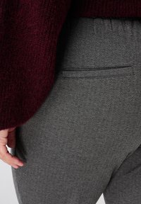 Grijze visgraatbroek met een achterzak en een subtiele stiksel. De stof is gestructureerd en past goed bij een bordeauxrood trui.