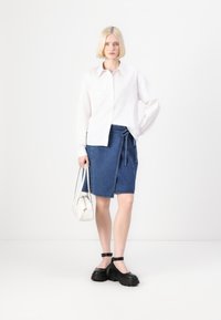 Hvit, brodert skjorte med knapper; blå denim omslagsskjørt; svarte kraftige sko; liten hvit håndveske. Enkelt, moderne design, nøytrale farger.