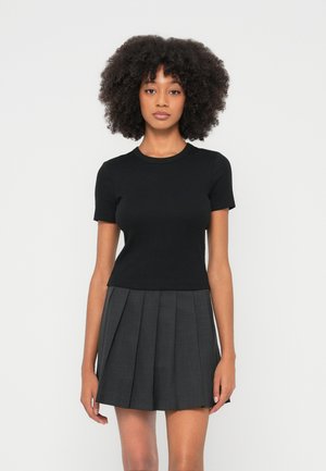 Czarna bluzka z krótkim rękawem o okrągłym dekolcie, zestawiona z plisowaną szarą spódnicą. Tkanina wydaje się gładka, a krój dopasowany.