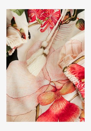 Tkanina w kwiatowy wzór z dużymi różowymi orchideami i czerwonym hibiskusem, z teksturowanymi marszczeniami i dekoracyjnymi frędzlami w kremowym kolorze z złotymi akcentami.