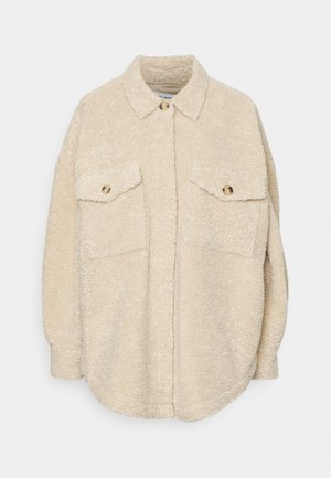 Beżowa polarowa koszula overshirt z kołnierzykiem, dwoma kieszeniami na piersi i złotymi guzikami. Miękka faktura i luźny fason. Okrągły dół.