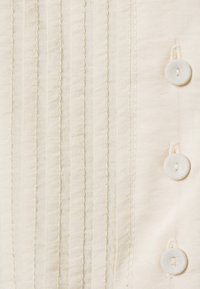 Tejido blanco roto con pliegues verticales, textura suave y tres botones de tela en el lado derecho.