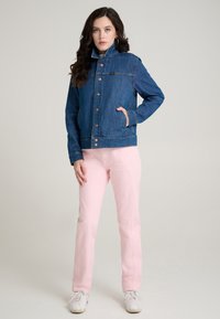 Tamsiai mėlynas džinsinis švarkelis su aukštu apykakliu, priekyje sagomis ir dviem šoninėmis kišenėmis. Derinamas su šviesiai rožiniais kelnėmis ir baltais batais.