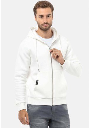 White zip-up hoodie made of soft fabric, featuring a kangaroo pocket, adjustable drawstrings, and ribbed cuffs, worn over a white T-shirt.
