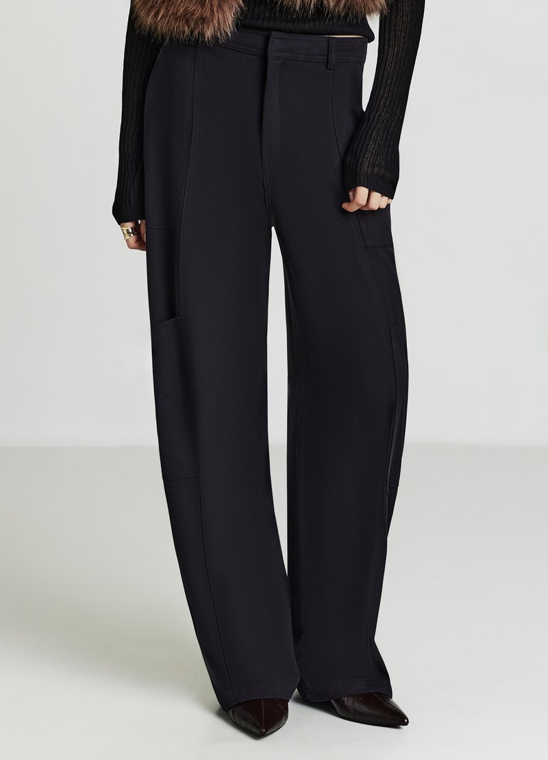 Schwarze Hose mit weitem Bein und glatter Textur, ausgestattet mit seitlichen Taschen und einem hoch taillierten Schnitt. Kombiniert mit einem schwarzen, gerippten Pullover.