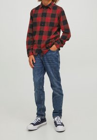 Rutig flanellskjorta i röd och svart med knappar, parat med blå denimjeans. Bärs med mörka sneakers och vita snören.