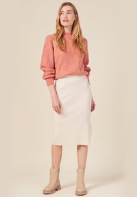 Sweater i mjuk korall med texturerad kabelstickning, ihop med en ribbad krämfärgad midikjol. Beiga ankelskor fulländar looken.