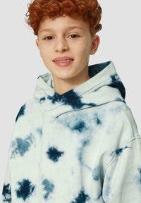 Mintgroene tie-dye hoodie met marineblauwe patronen, een trekkoordkap en een relaxte pasvorm. Zachte katoenen stof met zichtbare stikseldetails.