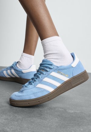 Blauwe suède sneakers met witte strepen en accenten, met een getextureerde bruine rubberen zool en gouden "Spezial" branding.