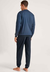 Marineblauwe pyjama set met een lange mouwen top met een sterrenpatroon, gecombineerd met effen donkere broek. Zacht materiaal, comfortabele pasvorm en elastische manchetten.