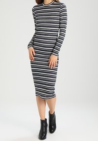 Robe à manches longues et ajustée avec des rayures horizontales bleu marine et blanches, dotée d'un col rond et d'une texture côtelée. Portée avec des bottines noires à la cheville.