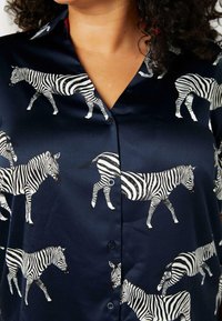 Mörkblå silkeskräm med ett zebramönster, knäppt framtill och med en slät yta. Zebrorna är avbildade i olika positioner.