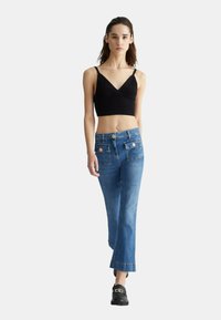 Top corto nero a coste con spalline regolabili, abbinato a jeans svasati azzurri chiari con ampie tasche frontali e dettagli in bottone dorato.
