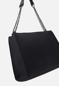 Černá kožená kabelka s texturovaným povrchem, geometrickým tvarem a stříbrným řetízkovým popruhem. Má horní zipové zapínání a strukturované strany.