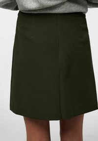 Olīvzaļš svārks ar taisnu griezumu, izgatavots no gludas auduma. Tam ir tīra apmale un tas ir paredzēts, lai nostāvētos tieši virs ceļa.