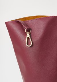 Maroon leather bag featuring a smooth texture, a metallic gold clasp, and contrasting yellow interior. Edge stitching is visible.