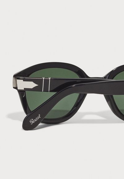 Occhiali da sole neri con lenti verdi, caratterizzati da un design elegante, dettagli in argento lucido e una tempia curvata incisa con la scritta "Persol."
