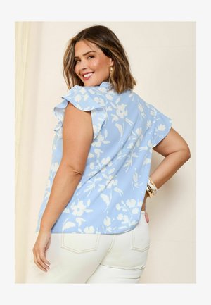 Svijetloplava cvjetna majica s kratkim volanima, s uzorkom bijelih cvjetova, nosi se s bijelim hlačama. Glatka tkanina i opušteni kroj.