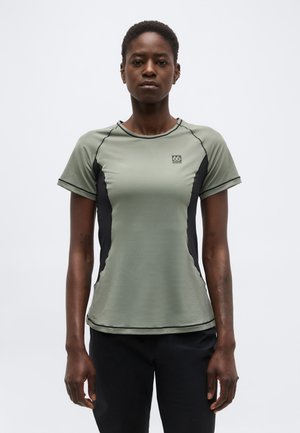 Kvinde står, iført en grå atletisk T-shirt med korte ærmer, sorte sidepaneler og logo på brystet, mod en ensartet hvid baggrund.