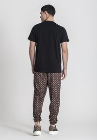 Čierne bavlnené tričko, hnedé jogger nohavice so vzorom a logom, elastické manžety a voľnočasové tenisky s hnedými a zelenými akcentmi.
